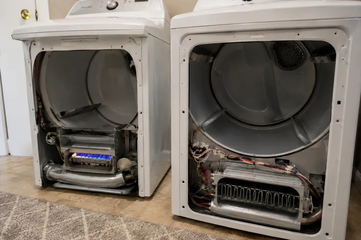 Disassembled gas and electric clothes dryers side-by-side during a diagnostic inspection, illustrating the complex internal components that require immediate appliance repair.