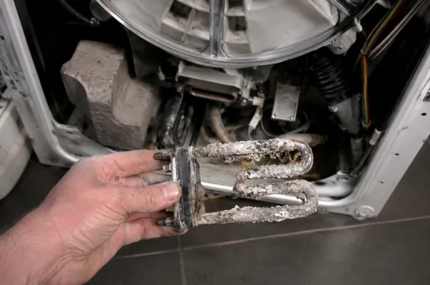 A technician holding a heavily corroded washing machine heating element covered in limescale, demonstrating the top signs your home needs immediate appliance repair due to hard water damage